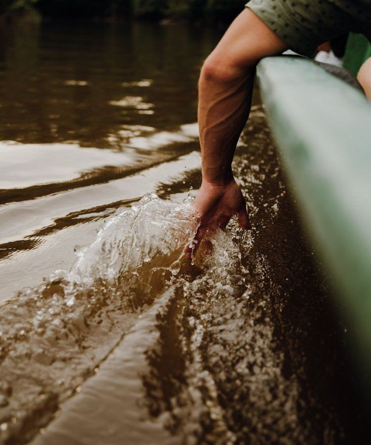 Foto de referencia: mano que roza el agua desde una canoa en movimiento.